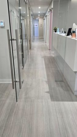 A clean, modern hallway with glass doors, white walls, and light wood flooring in a professional office setting.
