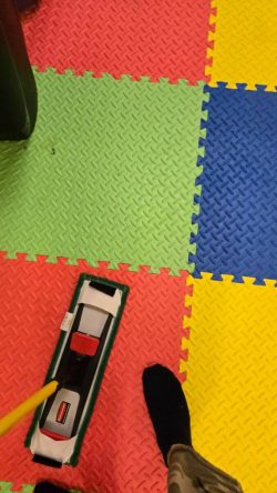 A person mops a colorful interlocking foam mat floor with red, green, blue, and yellow tiles.