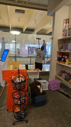 A person is cleaning a large glass window inside a toy and candy store with shelves of toys and snacks visible.