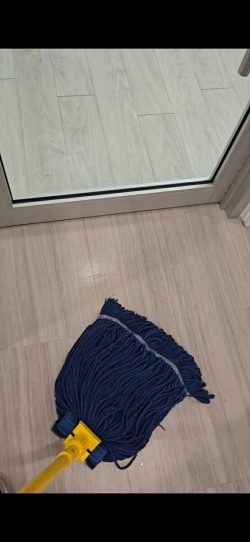 A blue mop with a yellow handle is on a light-colored tiled floor near a glass door.