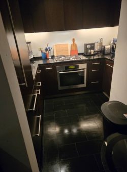 Modern kitchen with dark cabinets, black tile floor, built-in oven, and various appliances on the countertop.