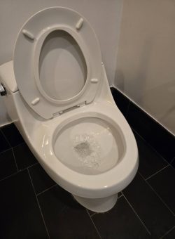 A white toilet with the lid up, flushing water visible inside the bowl, on a black tiled floor.