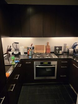 Modern kitchen with dark cabinets, built-in oven, countertop appliances, and various cooking utensils on the counter.