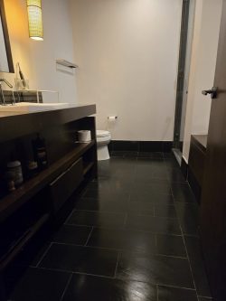 Modern bathroom with black tiled floor, a sink on a dark countertop, and a toilet near the back wall.